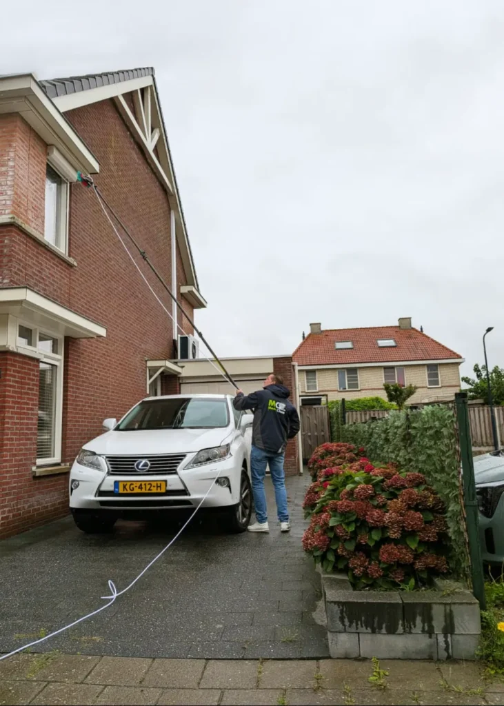 Erik van Mean Clean wast met een telescoopsteel en osmosewater een raam op de verdieping van een woning in Harlingen